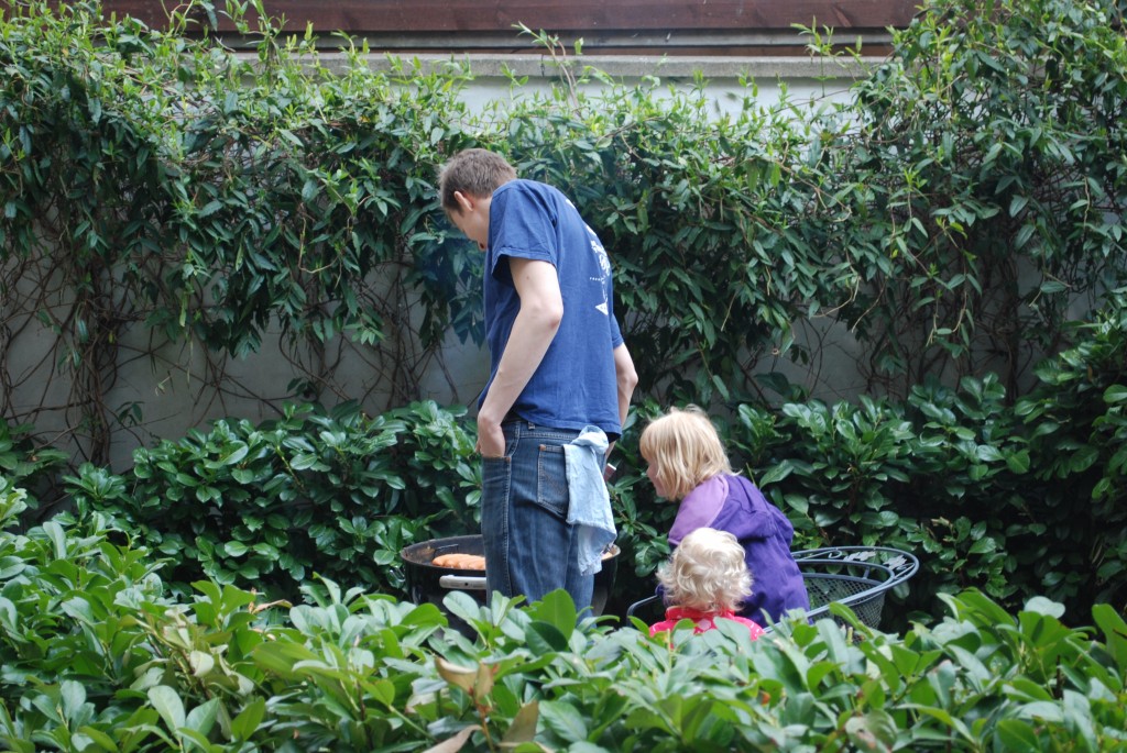 En far og 2 unge medhjælpere passer pølserne på grillen.