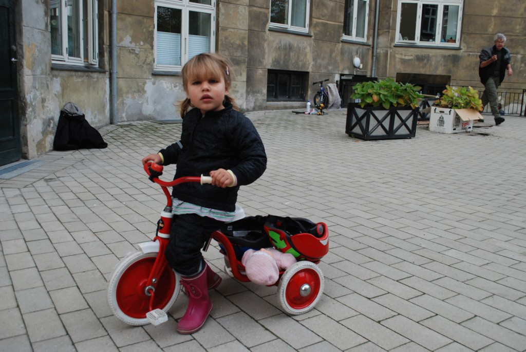 En pige på en tre-hjulet cykel kigger på fotografen.